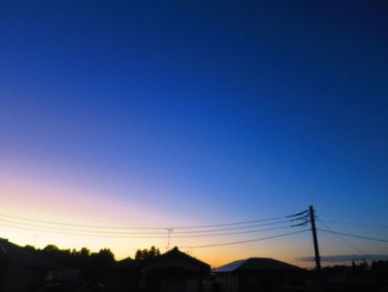 Low angle view of silhouette electricity pylons against sky at sunset