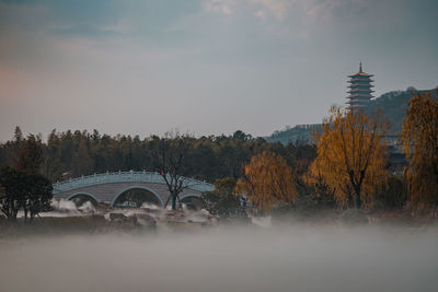 Arch bridge amidst trees and buildings against sky during autumn