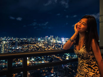 Woman standing by railing in illuminated city at night