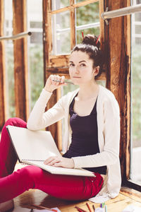 Portrait of woman sitting with book by window at home