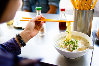 Cropped image of women eating noodles from chopsticks at restaurant