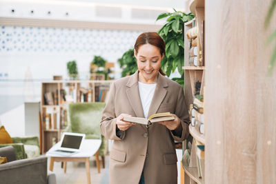 Adult smiling brunette business woman forty years in stylish beige suit and jeans at public place