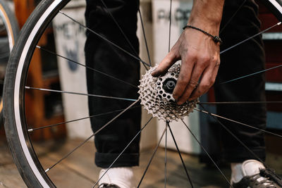 Crop anonymous male mechanic with dirty hands fixing gear cassette of wheel in repair workshop