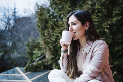 Young woman drinking coffee while sitting on tree