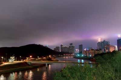 Illuminated buildings by river against sky at night