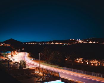 Light trails on road in city against sky at night