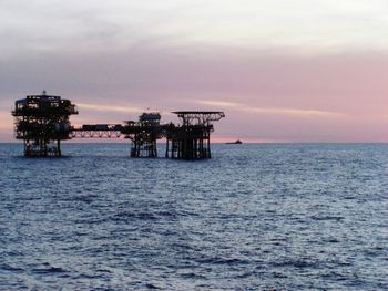 Silhouette built structure in sea against sky