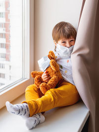 Boy with teddy bear in medical masks. kid with plush toy plays behind curtains.coronavirus covid-19.
