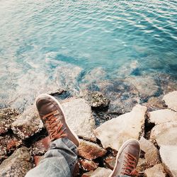 Low section of person relaxing on rock by sea