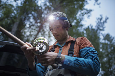 Low angle view of man holding fishing rod against trees