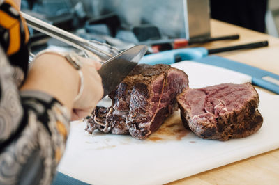 Midsection of woman cutting meat on board