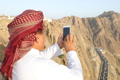 Midsection of man using mobile phone against mountains
