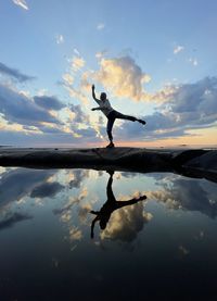 Silhouette man with reflection in lake against sky during sunset