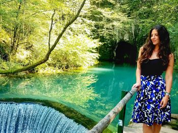 Young woman standing by lake against trees