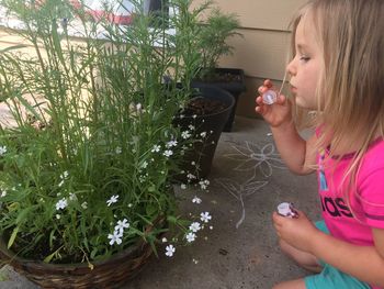 Side view of girl blowing bubbles by flowering plants on porch