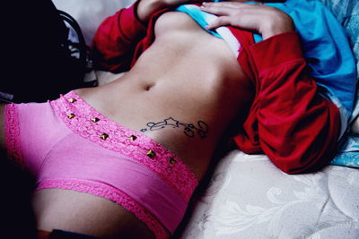 Midsection of sensuous woman wearing pink underwear while lying on bed