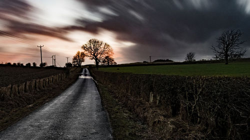 Road amidst agricultural field against sky during sunset