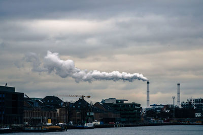 Smoke emitting from factory against cloudy sky