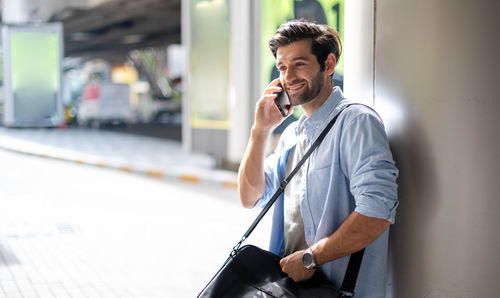 A young caucasian man watching the time and calling on his cell phone while waiting for his friend.