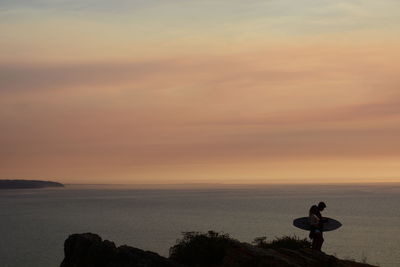 Silhouette man photographing sea against sky during sunset