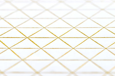 Gold diamond and triangle shaped lines engraved on white paper, selective focus.
