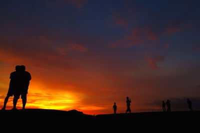 Silhouette people standing against orange sky