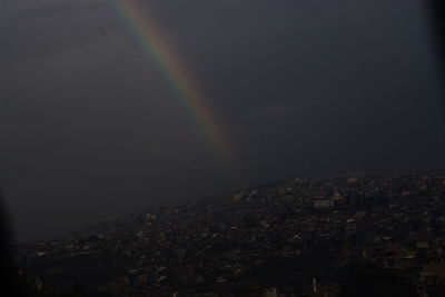 Rainbow over city against sky at night