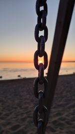 Close-up of chain on beach against sky during sunset