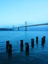 Wooden posts on river with oakland bay bridge in background against sky