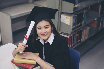 Smiling young woman in graduation gown holding diploma