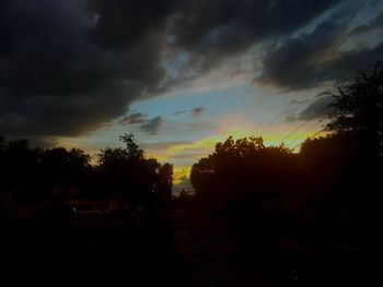 Silhouette trees on landscape against dramatic sky