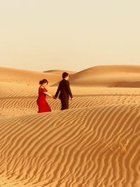 Couple on sand dune in desert against sky