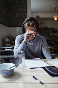 Teenage boy reading book while using headphones at home