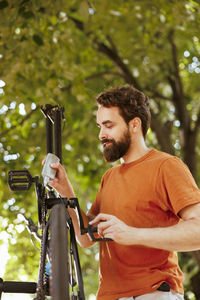 Young man with bicycle against trees