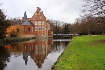 House by lake and buildings against sky