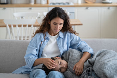 Good caring woman sits on sofa hugs girl teen lying on knees wrapped in warm blanket during illness