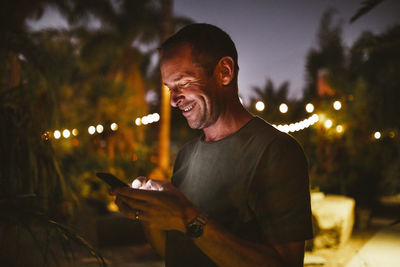 Smiling man using phone against sky during sunset