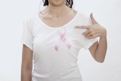 Midsection of woman pointing at breast cancer awareness ribbon against white background