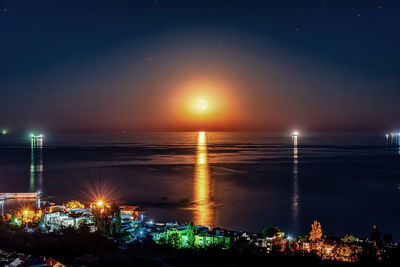 Illuminated city by sea against sky at night