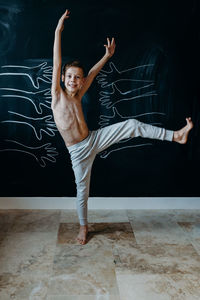 Portrait of shirtless boy dancing against wall