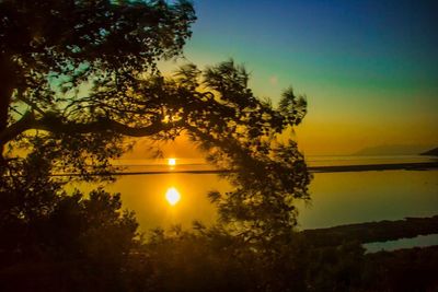 Silhouette trees by lake against sky during sunset