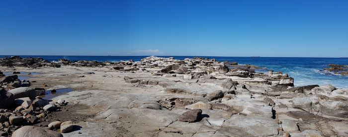 Scenic view of rocks on beach against clear blue sky