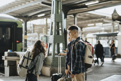 Side view of girl talking to brother while standing at waiting for train at railroad station