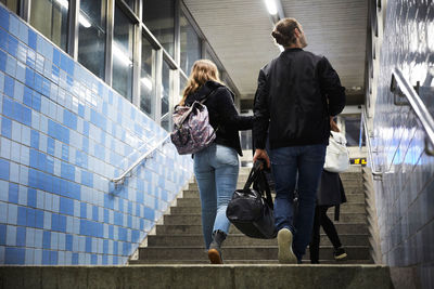 Full length of friends with luggage walking up on steps at subway station