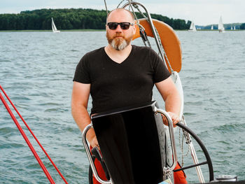 Handsome bearded person steering wheel sailing yacht on a lake in a cloudy summer day person