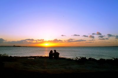 Silhouette people on beach against sky during sunset