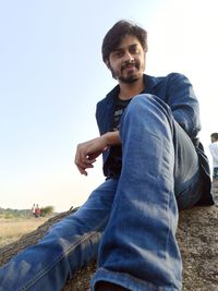 Portrait of young man sitting against clear sky