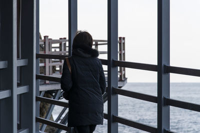 Rear view of woman standing by railing against sea