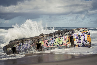 Waves rushing towards shore against cloudy sky