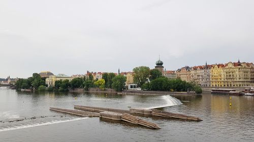 View of buildings by river against sky in city